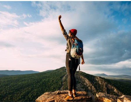 A male figure standing strong on a cliff edge with arms relaxed, gazing at majestic mountain views, representing the freedom and liberation that comes from inner child healing and learning to trust yourself.