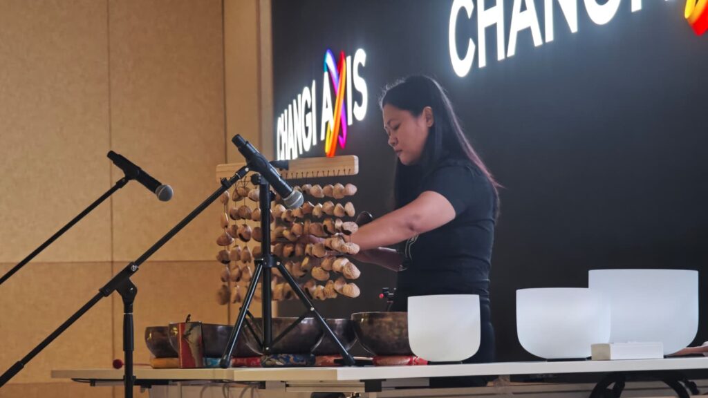 Sound practitioner playing nut seed chimes alongside singing bowls during a corporate sound bath session.