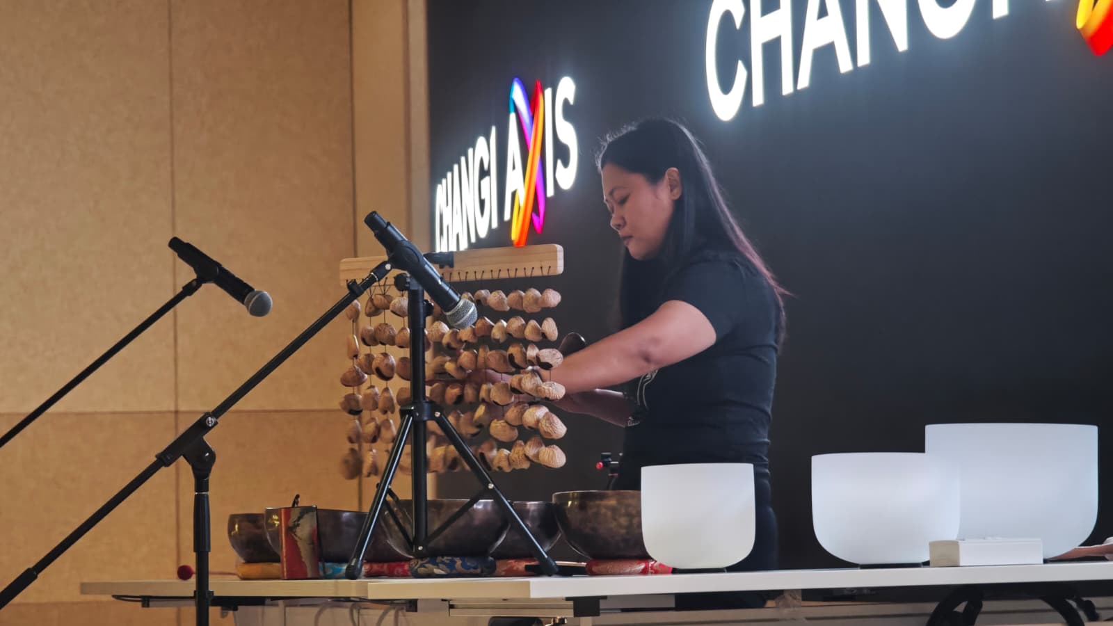 Sound practitioner playing nut seed chimes alongside singing bowls during a corporate sound bath session.