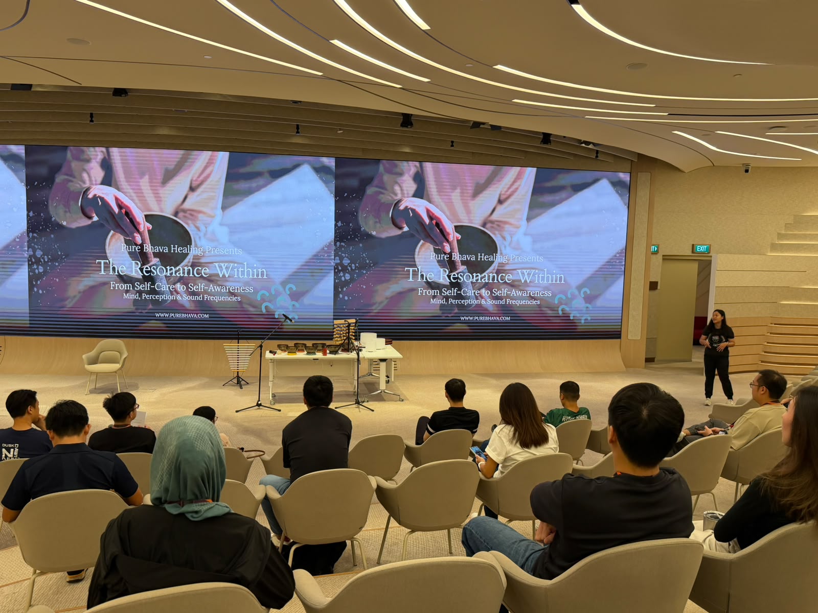 Sound healing and corporate wellness presentation titled "The Resonance Within: From Self-Care to Self-Awareness" in a modern auditorium.