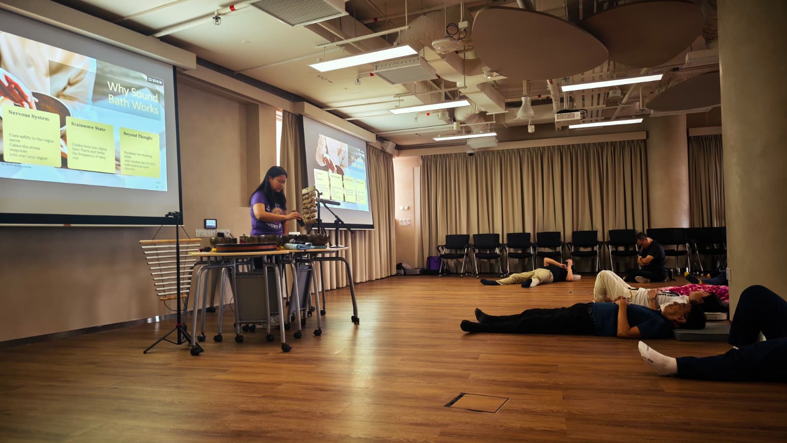 Sound bath practitioner playing instruments while participants lie down on mats during a workshop explaining why sound bath therapy works.